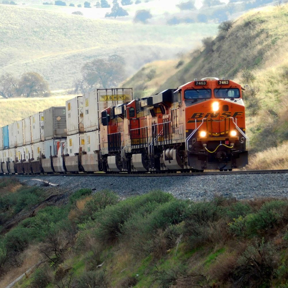 Freight train passing through scenic hills with vibrant landscape.